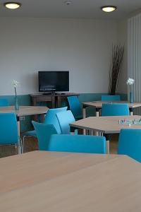 a room with tables and blue chairs and a flat screen tv at CVJM Jugendgästehaus Berlin in Berlin