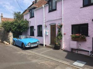 Red Rose Cottage في شيدر: سيارة زرقاء متوقفة أمام منزل أرجواني