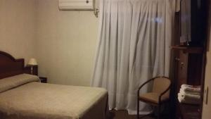 ein Schlafzimmer mit einem Bett und einem Stuhl neben einem Fenster in der Unterkunft Hotel Libertador in Santiago del Estero