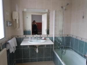 Eine Frau fotografiert ein Badezimmer mit Waschbecken und Badewanne in der Unterkunft Hôtel Le Bellevue Montrichard 3 étoiles in Montrichard