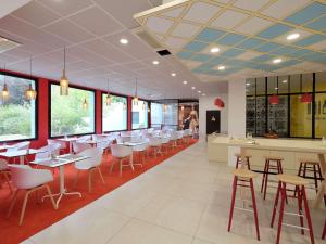 un restaurante con mesas y sillas blancas y ventanas en Hôtel ibis Styles Auxerre Nord, en Auxerre