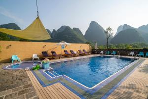 a pool with chairs and an umbrella and mountains in the background at The Giggling Tree in Yangshuo