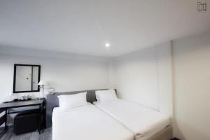 een witte kamer met een bed, een bureau en een spiegel bij Nana City Hotel in Bangkok