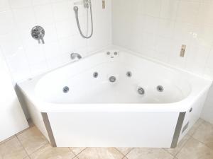 a white bath tub in a white tiled bathroom at Avalon Manor Motel in Motueka