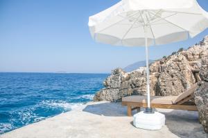 a chair with an umbrella on the edge of the ocean at Sunset Villa Hotel in Kaş