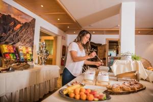 a woman is standing behind a table with food at Wirtshaushotel Alpenrose in San Lorenzo di Sebato
