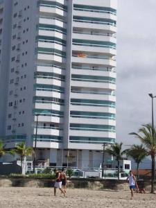 a group of people walking on the beach with a tall building at VILA CAIÇARA-FRENTE P/MAR in Solemar