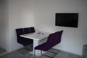 a white table with purple chairs and a tv on a wall at Apartments "NONO" in Mlini
