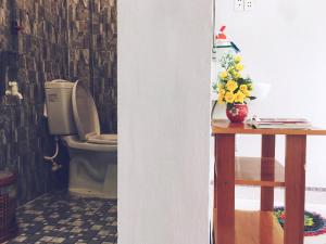 a bathroom with a toilet and a table with a vase of flowers at Trang Vu Homestay Cu Lao Cham in Tân Hiệp