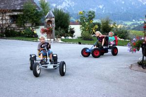 three children riding on toy cars in a driveway at Familienbauernhof Christa in Rossleithen