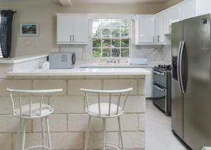 eine Küche mit weißen Schränken und einem Kühlschrank aus Edelstahl in der Unterkunft Ez Living Apartments in Bridgetown
