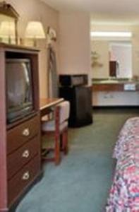 Habitación de hotel con TV, cama y escritorio. en Red Carpet Inn Macon East, en Macon