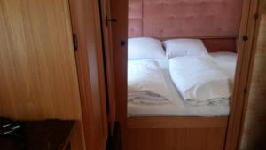 uma pequena cama com lençóis brancos e almofadas em Caravans Magda em Niechorze
