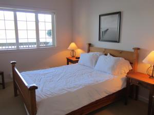 a bedroom with a bed with white sheets and two lamps at 203 at Water's Edge in Ucluelet