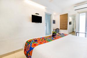 Un dormitorio con una cama blanca con una colorida manta estampada en FabExpress Kalyan, en Vadodara