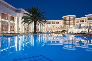 una piscina de hotel con una palmera frente a un edificio en Mythos Palace Resort & Spa en Georgioupolis