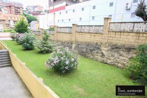 un jardín con flores en el césped junto a una pared en Enjoy Santander, en Santander