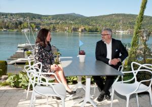 Ein Mann und eine Frau sitzen an einem Tisch an einem See in der Unterkunft Tennis & Yacht Hotel Velden in Velden am Wörthersee