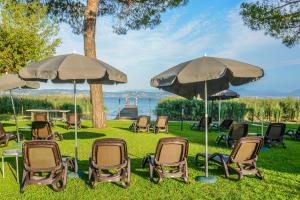 un groupe de chaises et de parasols dans l'herbe dans l'établissement Hotel Miramar, à Sirmione