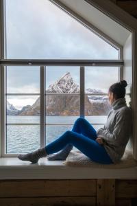 
a woman sitting on a window ledge looking out at the ocean at Olstind in Sakrisøy in Reine
