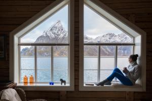 a woman sitting on a window sill looking out at the mountains at Olstind in Sakrisøy in Reine