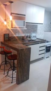 a kitchen with white cabinets and a counter with stools at Apartamento Ed. Ouro Preto Praia do Morro in Guarapari