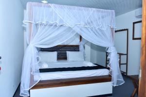 1 dormitorio con cama con dosel y cortinas blancas en Silent River Cottage en Udawalawe
