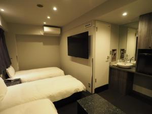 Habitación de hotel con 2 camas, lavabo y TV. en Haneda Inn en Tokio