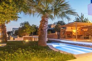 a swimming pool with a palm tree next to a house at Porto Bello Tinos in Agios Ioannis