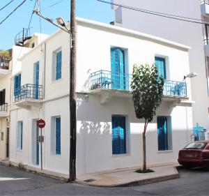 a white building with blue windows and a tree on a street at Marika's Traditional House in Agios Nikolaos