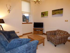 uma sala de estar com um sofá e uma cadeira e uma televisão em The Pipers No 7 Lomond Castle em Balloch