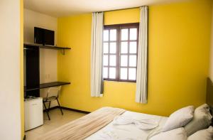 um quarto amarelo com uma cama e uma janela em Hotel Pousada Trevo em Jequié