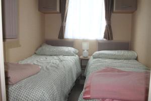 two beds in a small bedroom with a window at The Valley Static Caravan in Pembrokeshire