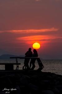 una pareja sentada en un banco frente a la puesta de sol en Atardecer porteño, en Puntarenas