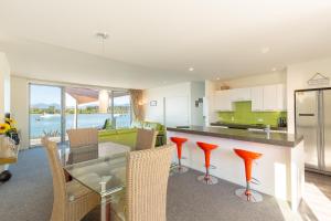 Mapua Wharfside Apartments في Mapua: مطبخ مع طاولة زجاجية وكراسي حمراء