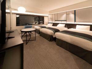 una camera d'albergo con tre letti e una televisione di Hotel Vischio Osaka-JR Hotel Group ad Osaka