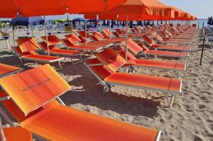 a row of orange beach chairs and umbrellas on a beach at Al-Tair in San Vito lo Capo
