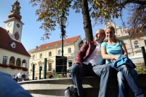 Un uomo e una donna seduti su una panchina di fronte a un edificio di Hotel Babenbergerhof a Mödling