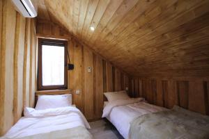 two beds in a room with wooden walls and a window at Domek Fiona in Boszkowo