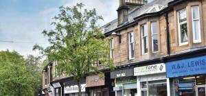 eine Straße mit Geschäften und einem Baum vor einem Gebäude in der Unterkunft West Highland Apartments Milngavie - The Lomond in Milngavie