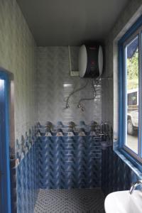 baño de azulejos azules con lavabo y ventana en Vamoose Sherpa Homestay, en Ravangla