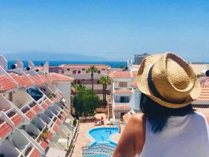 a woman wearing a straw hat looking out at a swimming pool at Penthouse las Flores in Playa de las Americas