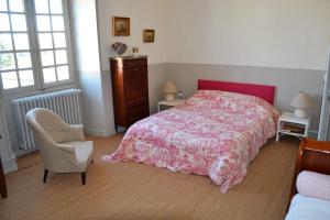 a bedroom with a bed and a chair and two windows at Le Petit Logis in Rouillac