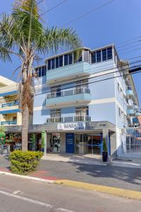 a tall white building with a palm tree in front of it at Marazul Apart Hotel in Florianópolis