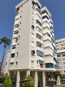 un edificio de apartamentos alto y blanco con una palmera en Playa Dos Avenidas en Alicante