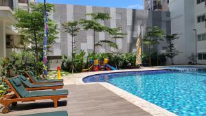 a swimming pool with two lounge chairs and a playground at Studio Signature Park Grande Apartment Near MT Haryono By Travelio in Jakarta