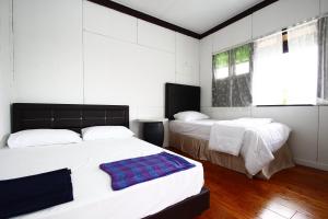 2 camas en un dormitorio con paredes blancas y suelo de madera en The Green Cottage, en Kuching