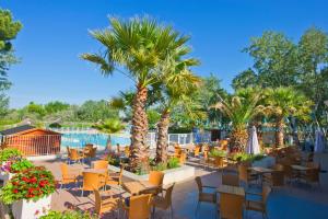 d'une terrasse avec des tables, des chaises et des palmiers. dans l'établissement Azureva Le Grau du Roi, au Grau-du-Roi