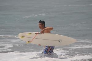 un hombre de pie en el océano sosteniendo una tabla de surf en Dabumito Guest House, en Canggu