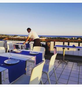 un hombre de pie en un balcón con mesas y sillas en L'Angolo Di Beppe en Torre Lapillo